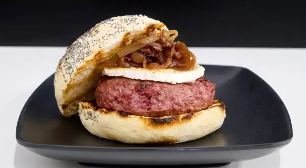 Deliciosa hamburguesa de ternera con queso de cabra y cebolla caramelizada, servida en pan con semillas de amapola.