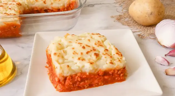 Un delicioso pastel de patata y carne, cubierto con puré de patatas dorado y servido en un plato blanco.