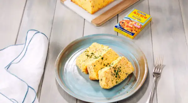Rebanadas de pastel de pescado, esponjoso y dorado, servido en plato azul. Acompañado de un caldo de pescado.
