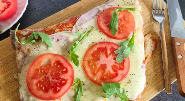 Un delicioso matambre a la pizza, cubierto de queso derretido, rodajas de tomate fresco y rúcula, servido en tabla de madera.