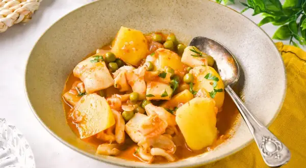 Un plato humeante de patatas con sepia de la abuela, con guisantes y perejil fresco.