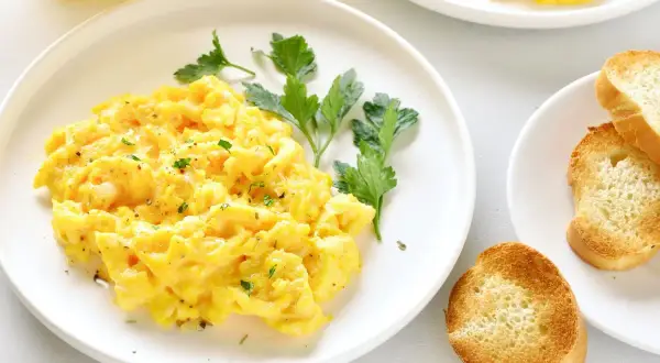 Un plato de huevos revueltos esponjosos, adornado con perejil fresco y acompañado de tostadas crujientes.
