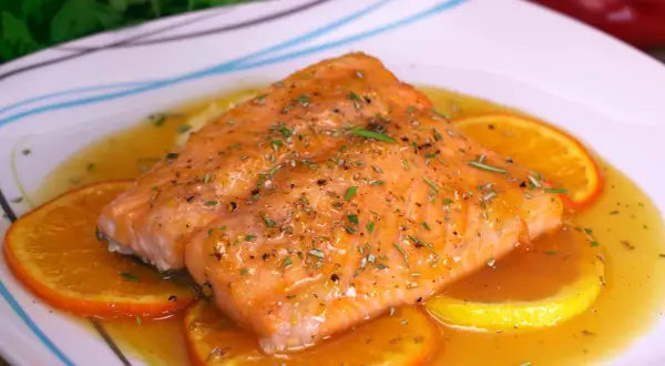 Delicioso salmón a la naranja, bañado en salsa cítrica y adornado con rodajas de naranja y hierbas frescas.