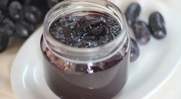 Frasco de mermelada de uvas casera, con uvas frescas al lado. Un dulce manjar para disfrutar.