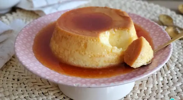 Un delicioso flan de leche condensada, con una porción servida en cuchara dorada, bañado en caramelo líquido.