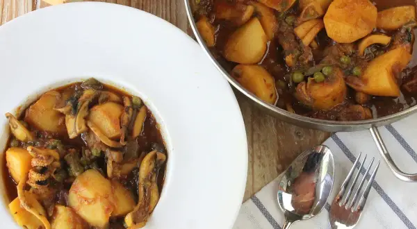 Plato de papas con choco y guisantes en salsa, servido en un cuenco blanco. Al lado, una sartén con el mismo guiso.