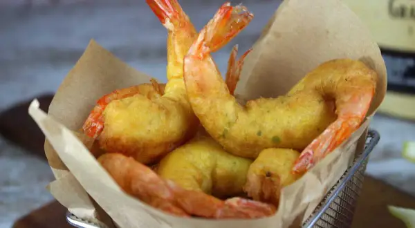 Crujientes gambas a la gabardina doradas, servidas en una cesta metálica con papel marrón.