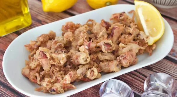 Crujientes puntillas de calamar fritas, servidas en plato blanco con limón y aceite de oliva.
