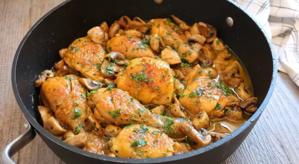 Pollo a la cerveza jugoso y dorado, con champiñones y perejil fresco, servido en una sartén.