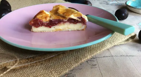Rebanada de pastel vasco con relleno de crema y mermelada de frutos rojos, servida en plato rosa.