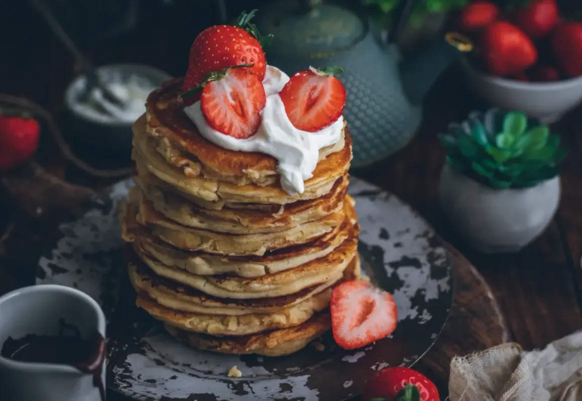 Pila de tortitas esponjosas cubiertas con nata y fresas. Una deliciosa receta de tortitas para el desayuno.