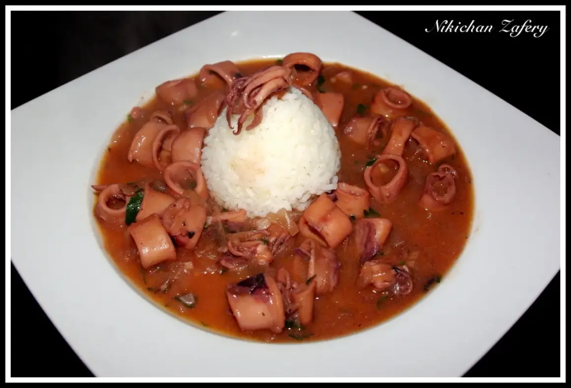 Calamares encebollados en una salsa rojiza, servidos con una bola de arroz blanco en un plato blanco.
