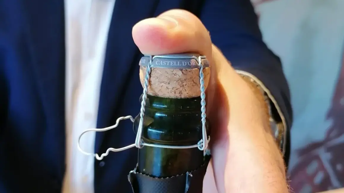 Dedo presionando el corcho de una botella de cava "CASTELL D'OR". Aprende como abrir una botella de vino espumoso.