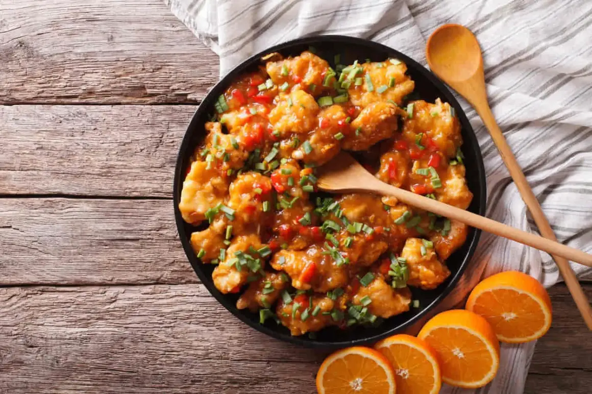 Delicioso pollo a la naranja, crujiente y bañado en una salsa dulce y cítrica, adornado con cebollín fresco.