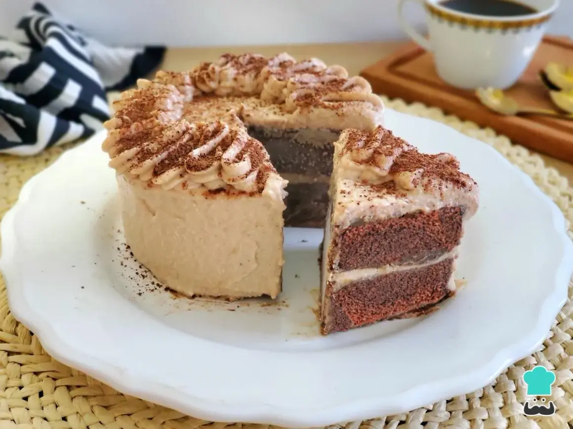 Deliciosa tarta de moka con crema y cacao espolvoreado. Un trozo cortado revela sus capas de bizcocho y relleno.