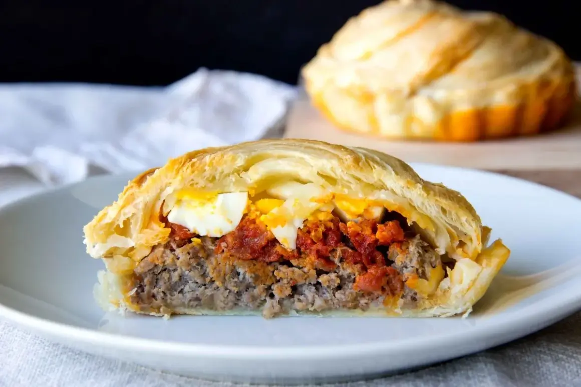 Un trozo de pastel de carne murciano, relleno de carne picada, tomate y huevo duro, envuelto en hojaldre dorado.