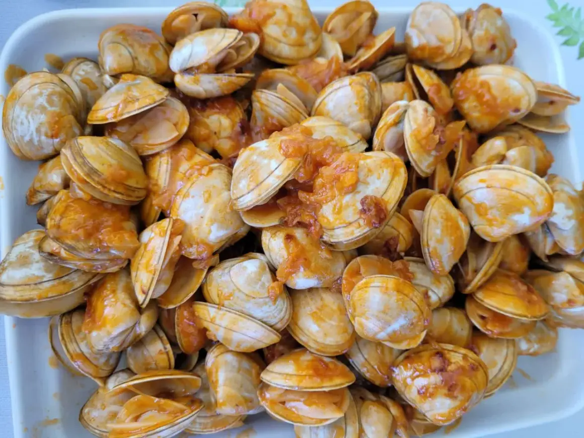 Un plato rebosante de almejas a la marinera, con su salsa anaranjada cubriendo las conchas.