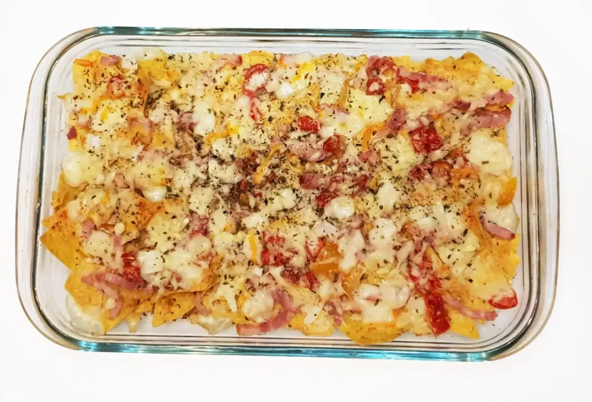Nachos con queso recién horneados, cubiertos con trozos de tocino y pimientos rojos.
