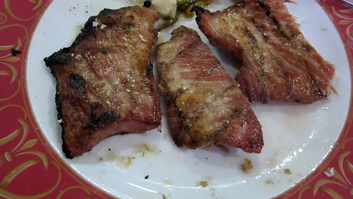 Tres jugosas porciones de secreto ibérico a la parrilla, con sal gruesa y un toque de pimienta, servidas en un plato blanco con borde decorado.