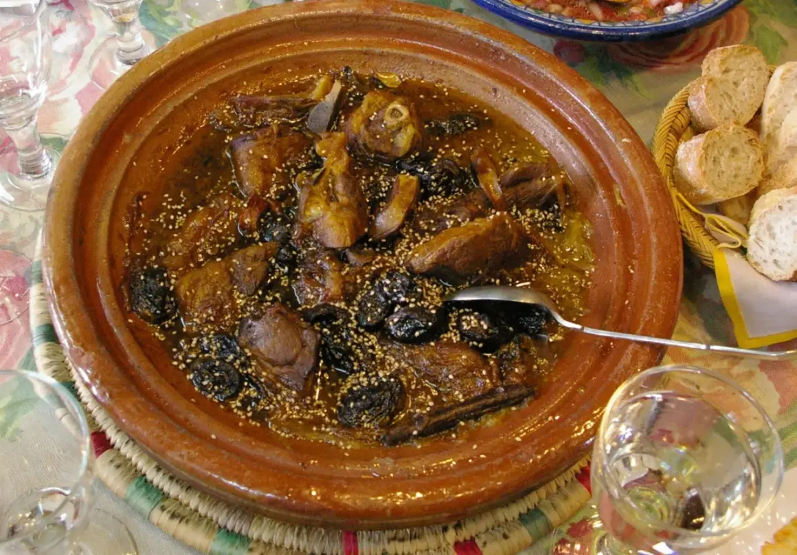 Un delicioso tajine de cordero con ciruelas pasas y semillas de sésamo, servido en una cazuela de barro.