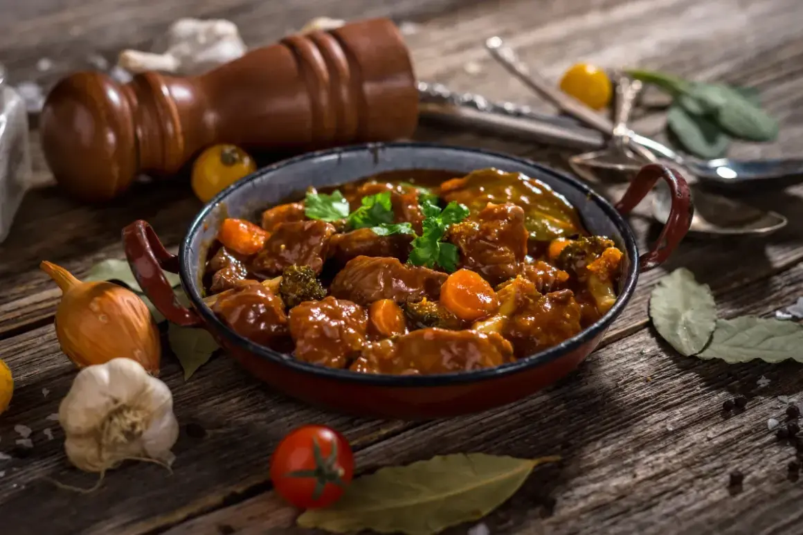 Un delicioso caldereta de cordero, con trozos tiernos de carne, zanahorias y brócoli, servido en una cazuela rústica.