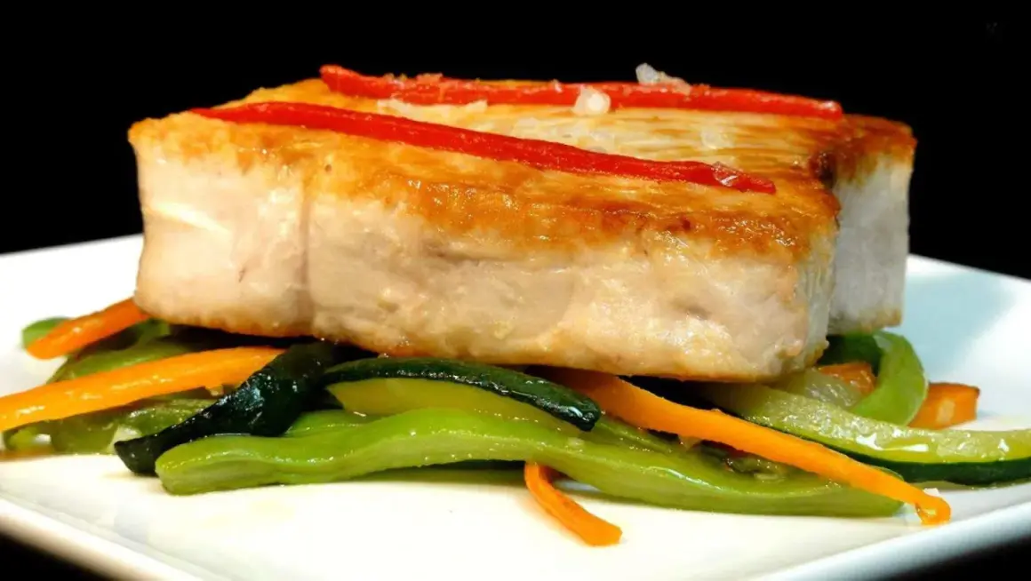Bonito jugoso sobre verduras salteadas, con tiras de pimiento rojo.