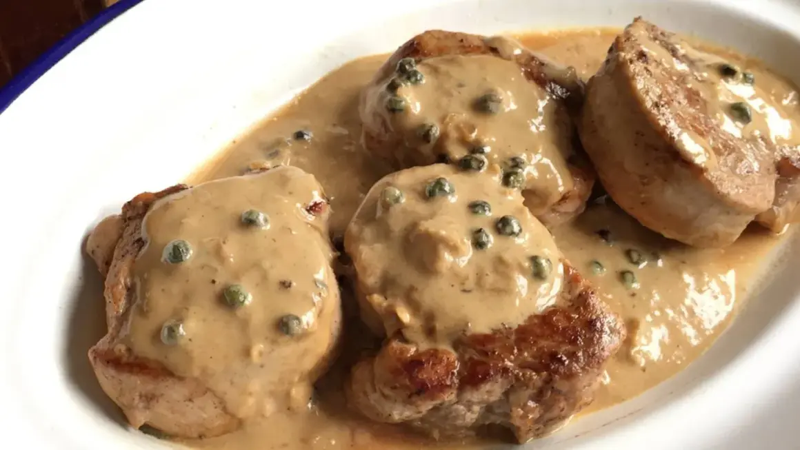 Cuatro medallones de solomillo a la pimienta, cubiertos con una cremosa salsa de pimienta verde, servidos en un plato blanco.