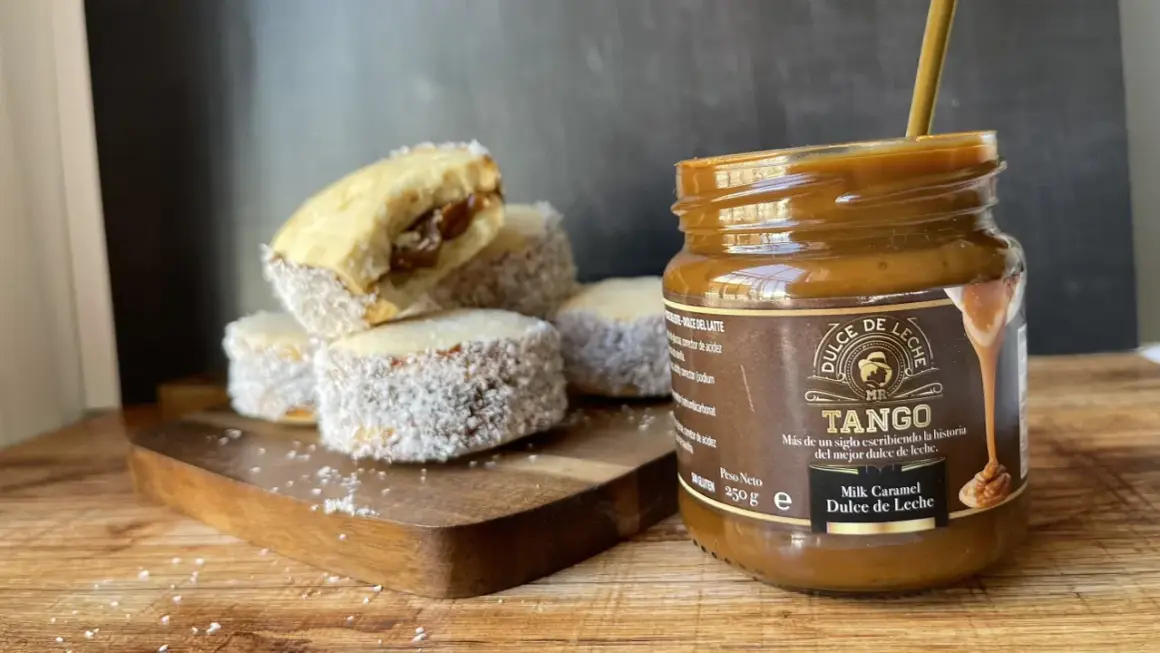 Alfajores cubiertos de coco y un frasco de dulce de leche Tango, listos para disfrutar.