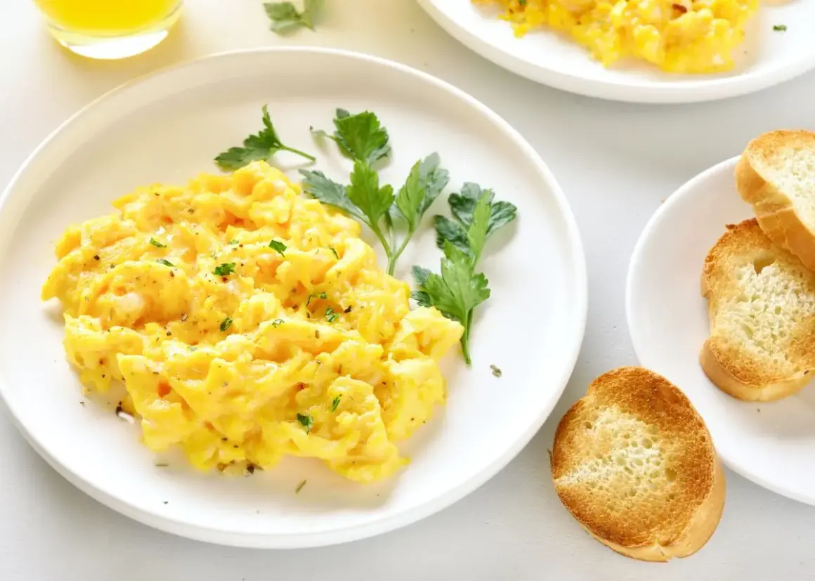 Un plato de huevos revueltos esponjosos, adornado con perejil fresco y acompañado de tostadas crujientes.