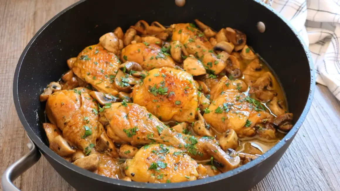 Pollo a la cerveza jugoso y dorado, con champiñones y perejil fresco, servido en una sartén.