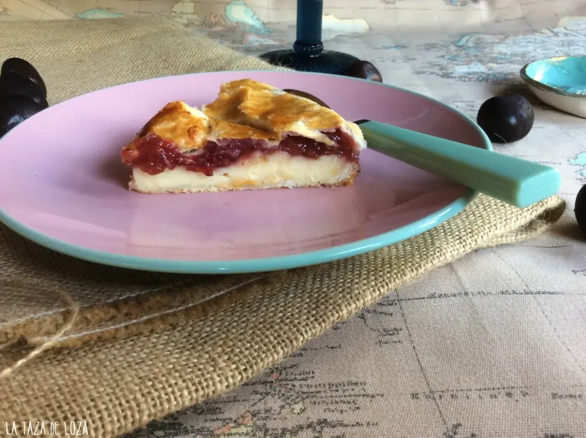Rebanada de pastel vasco con relleno de crema y mermelada de frutos rojos, servida en plato rosa.
