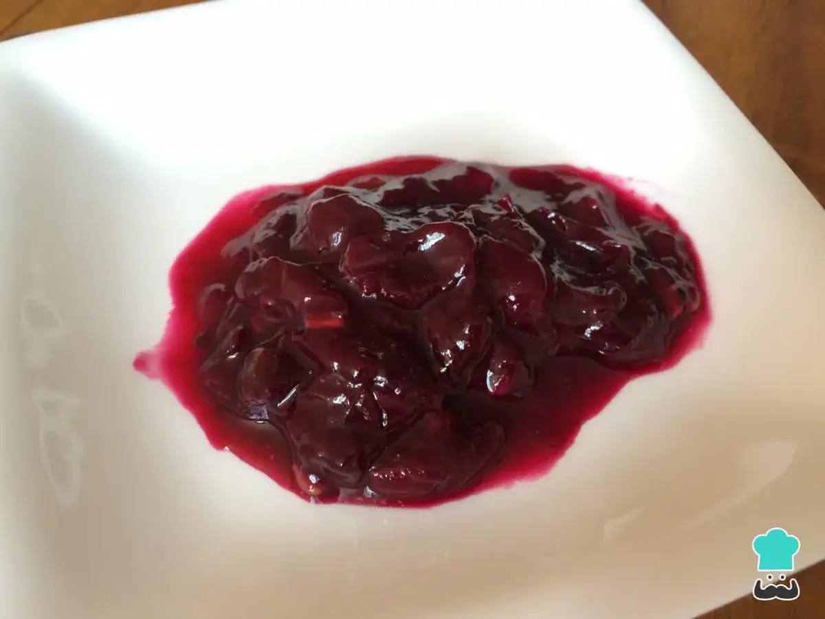 Mermelada de uvas casera, oscura y brillante, servida en un plato blanco.