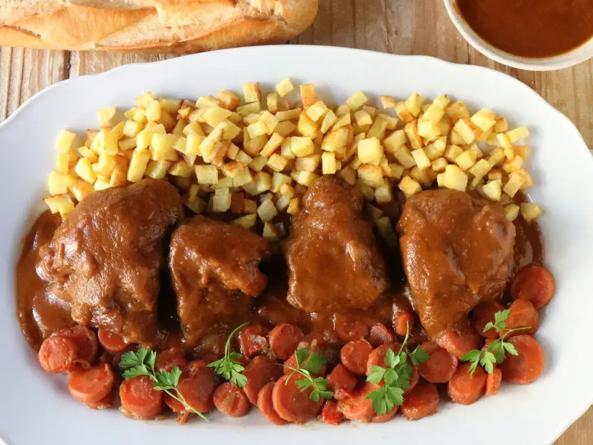 Delicioso jarrete de ternera estofado en salsa, acompañado de patatas fritas y zanahorias.