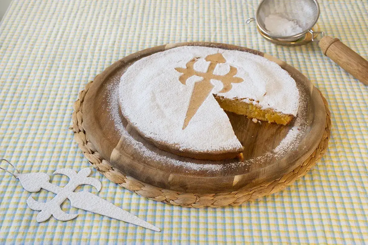 Tarta de Santiago, espolvoreada con az&uacute;car glas y decorada con la Cruz de Santiago. Una porci&oacute;n ha sido retirada, revelando su interior dorado.