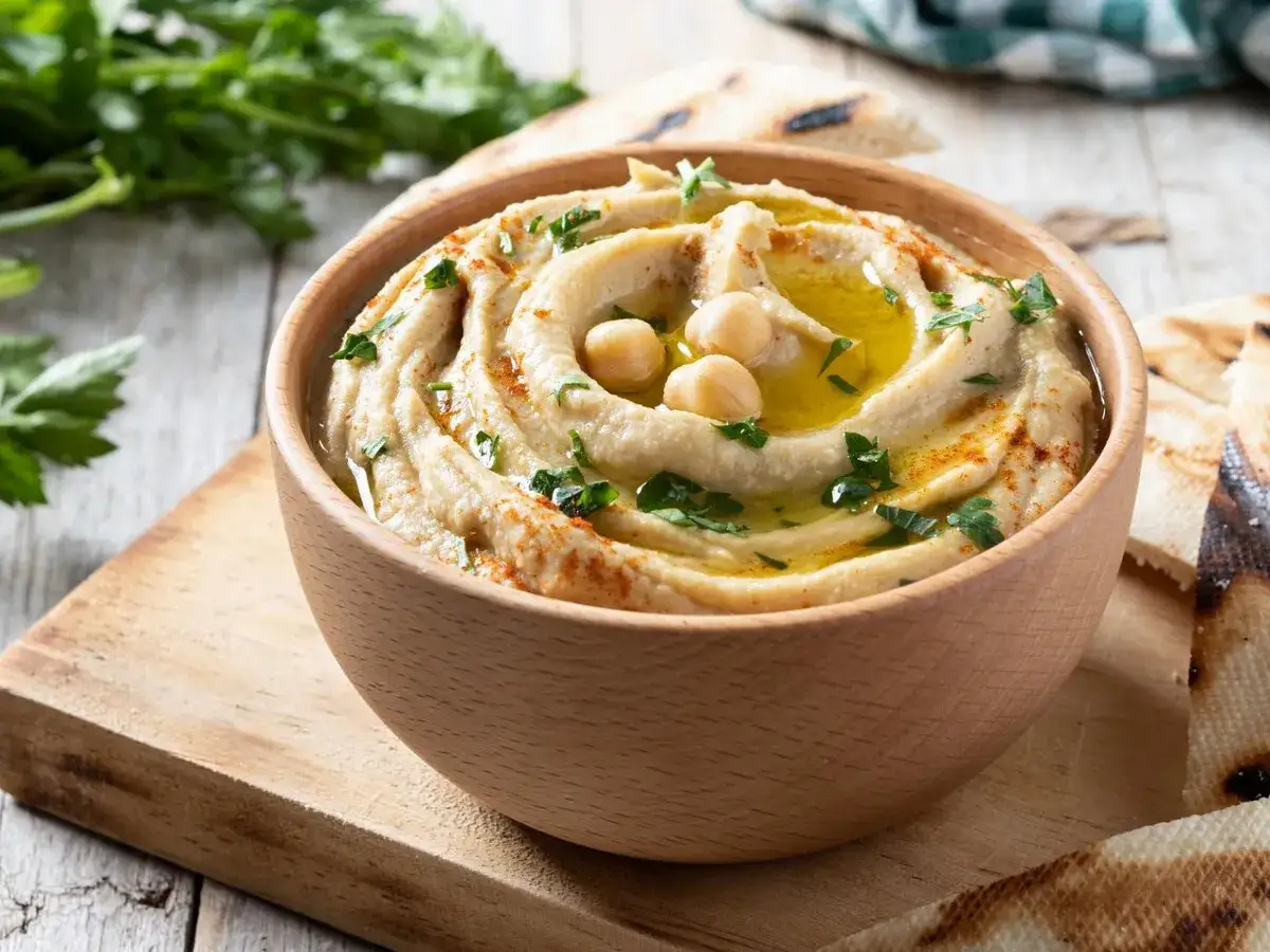 Un cremoso hummus casero, perfecto para tu pr&oacute;xima hummus receta, servido en un cuenco de madera con garbanzos y piment&oacute;n.