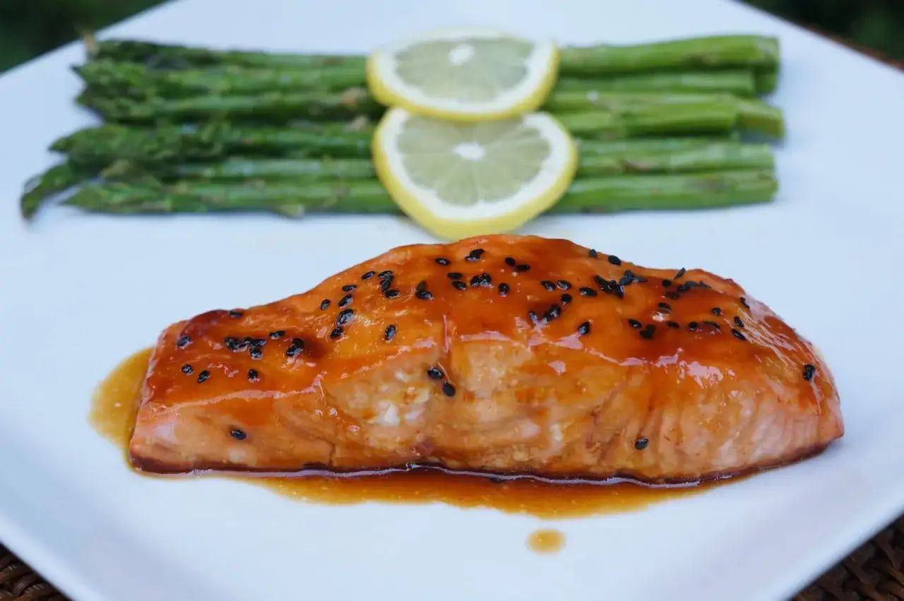 Filete de salmón a la naranja glaseado con semillas negras, acompañado de espárragos y rodajas de limón.
