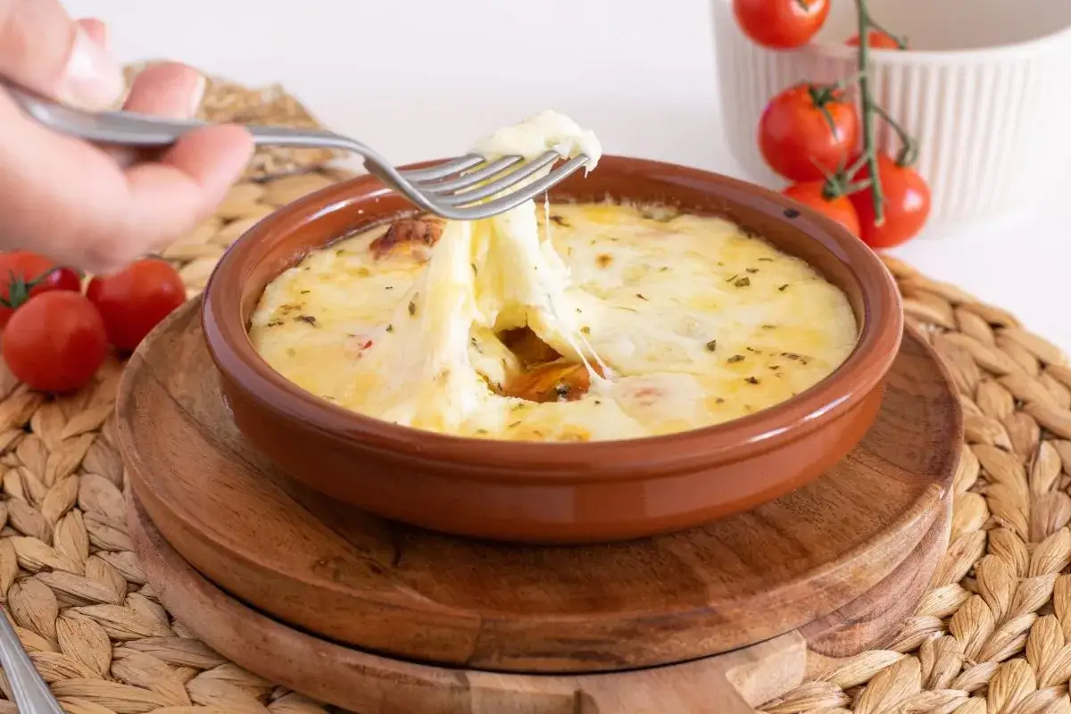 Un tenedor saca queso fundido de un plato de provolone al horno, con tomates cherry al lado.