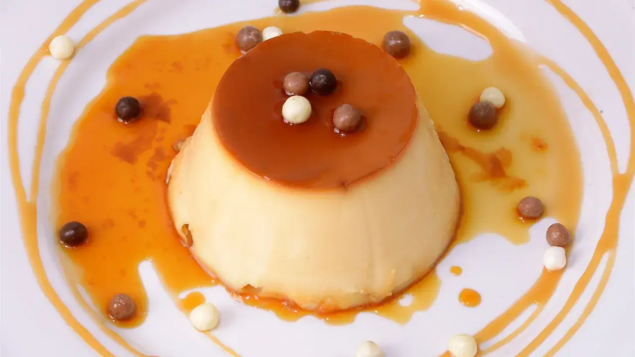Delicioso flan de leche condensada ba&ntilde;ado en caramelo l&iacute;quido y decorado con bolitas de chocolate y crema.
