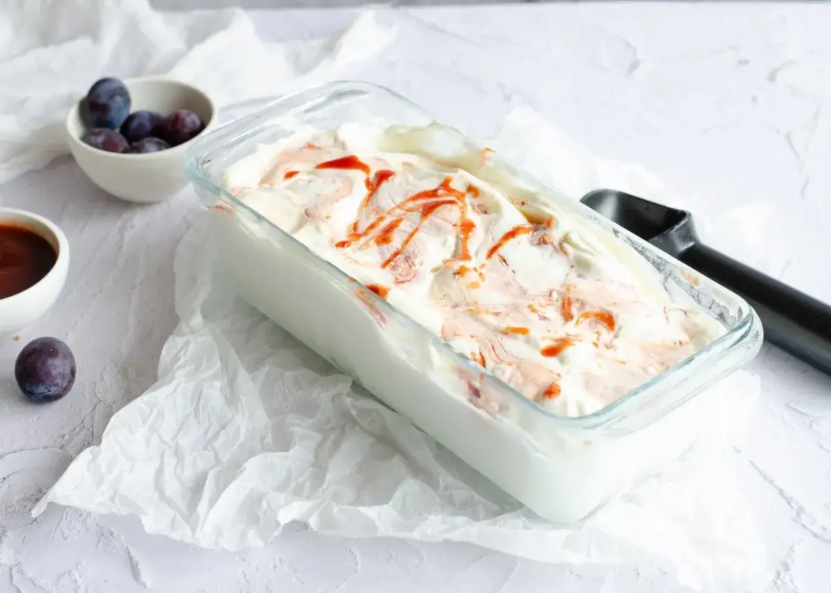 Delicioso helado de queso con remolinos de mermelada de ciruela y una cuchara lista para servir.