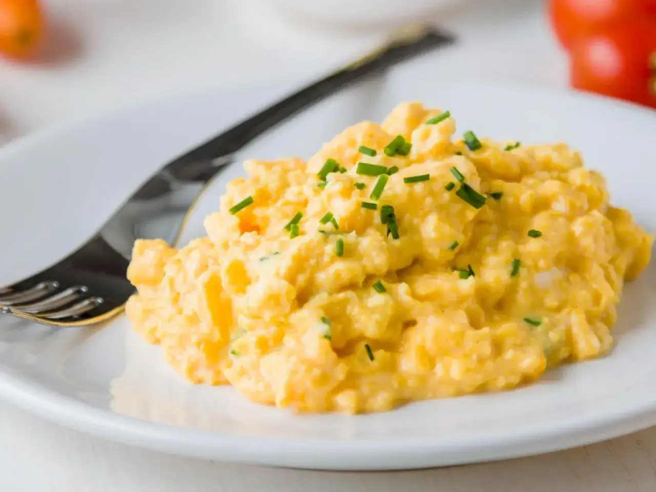 Un plato de huevos revueltos cremosos, adornados con cebollino fresco, listos para disfrutar.