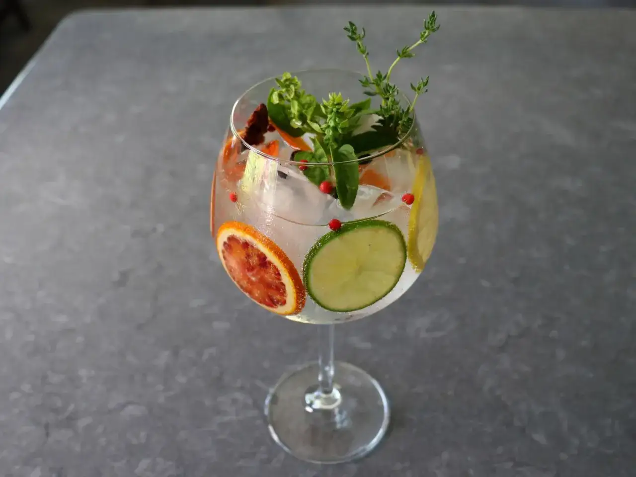 Un refrescante gin tonic con rodajas de naranja sanguina, lima y limón, adornado con hierbas y bayas. Así es que es la ginebra.