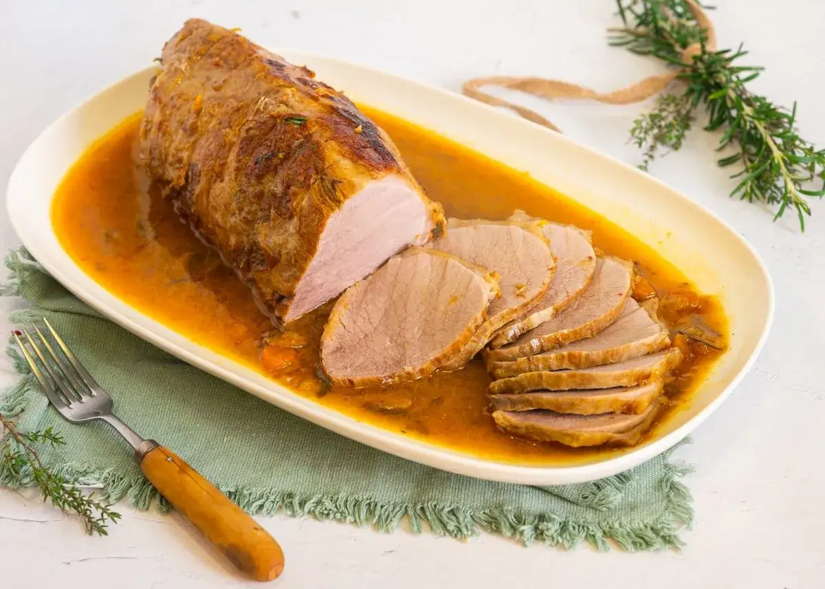Cerdo redondo en salsa dorada, jugoso y tierno, servido en una bandeja ovalada con rodajas listas para disfrutar.