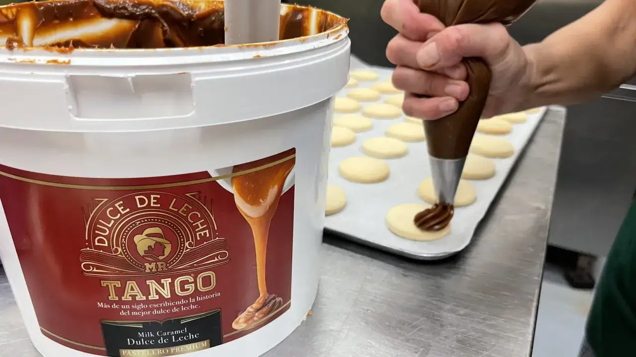 Un repostero decora galletas con dulce de leche cremoso, sacado de un gran balde de
