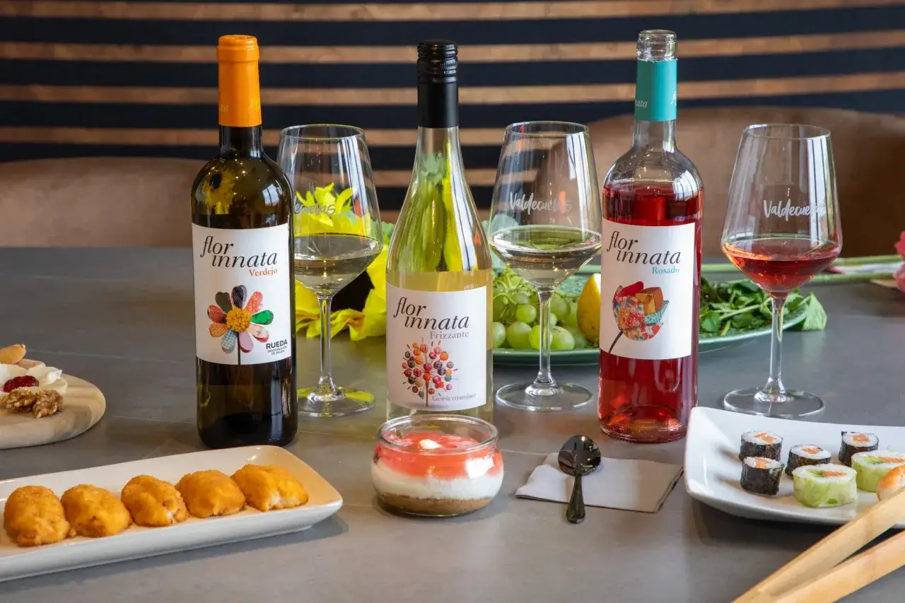 Tres botellas de vino, una blanca, una rosada y una frizzante, acompañadas de croquetas, sushi y un postre.