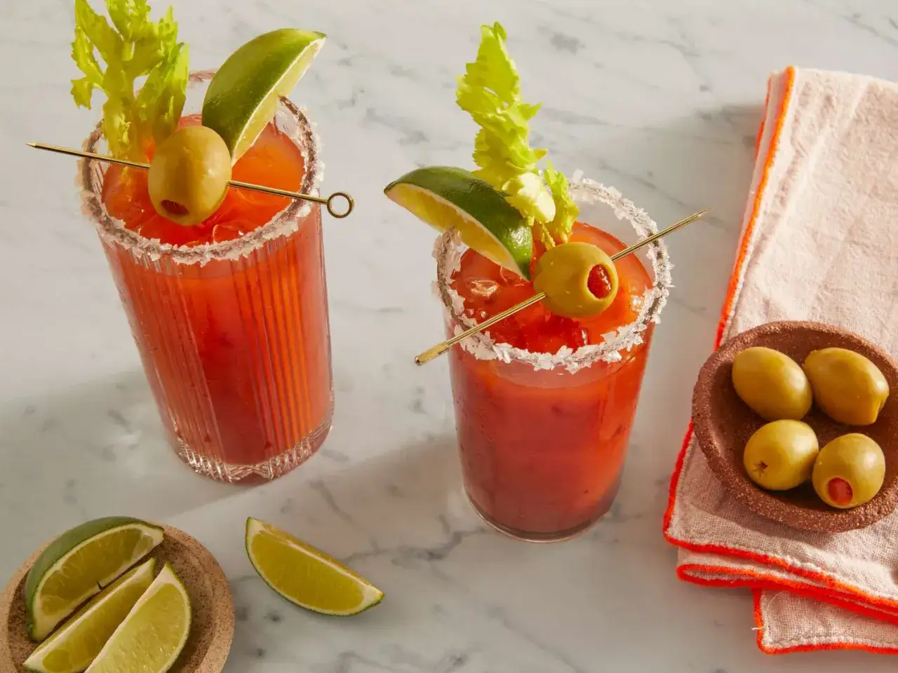 Dos Bloody Marys listos para disfrutar. Aprende como hacer bloody mary con apio, lima y aceitunas.