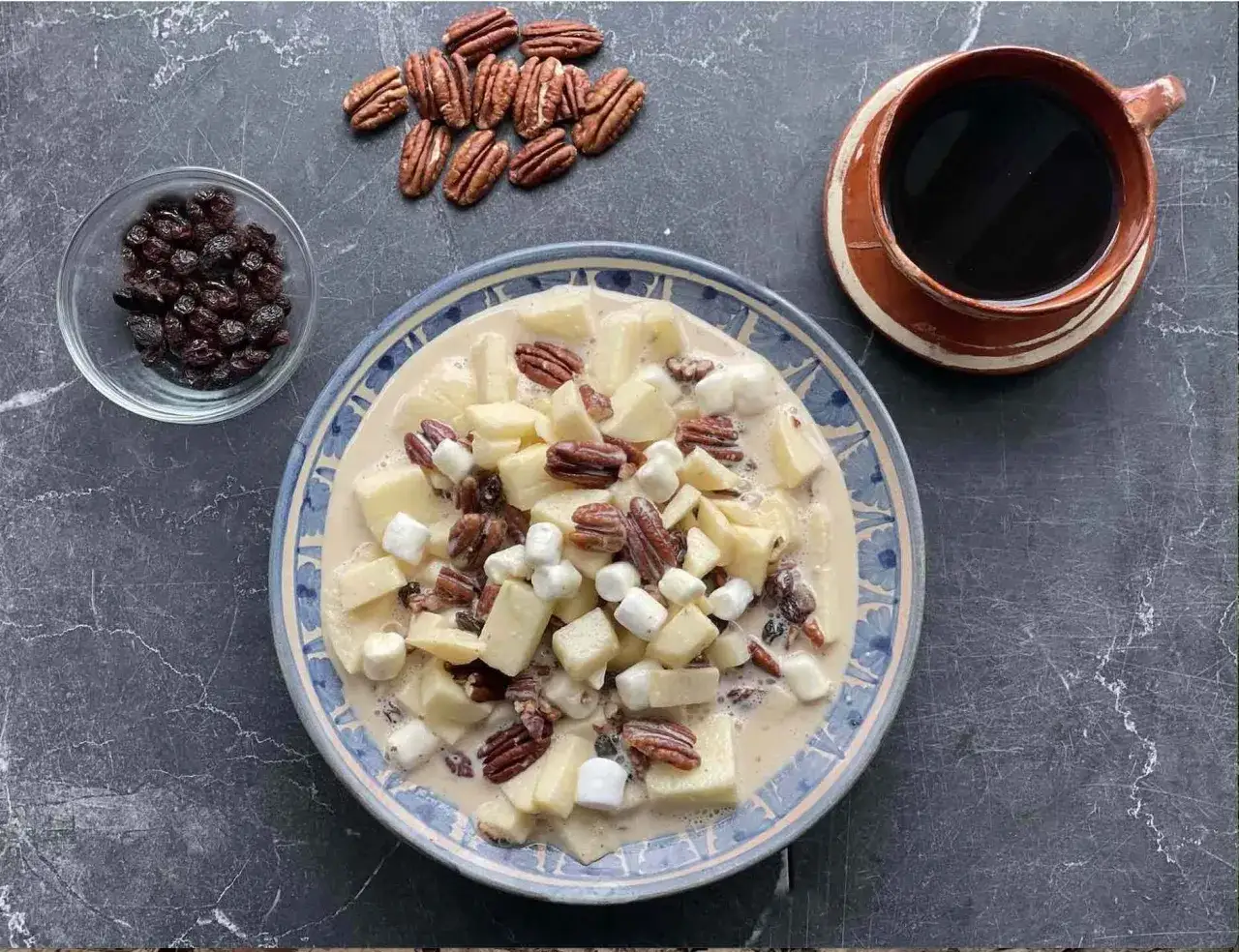 Delicioso pudin de manzana con nueces pecanas, pasas y malvaviscos. Una taza de café acompaña este postre.