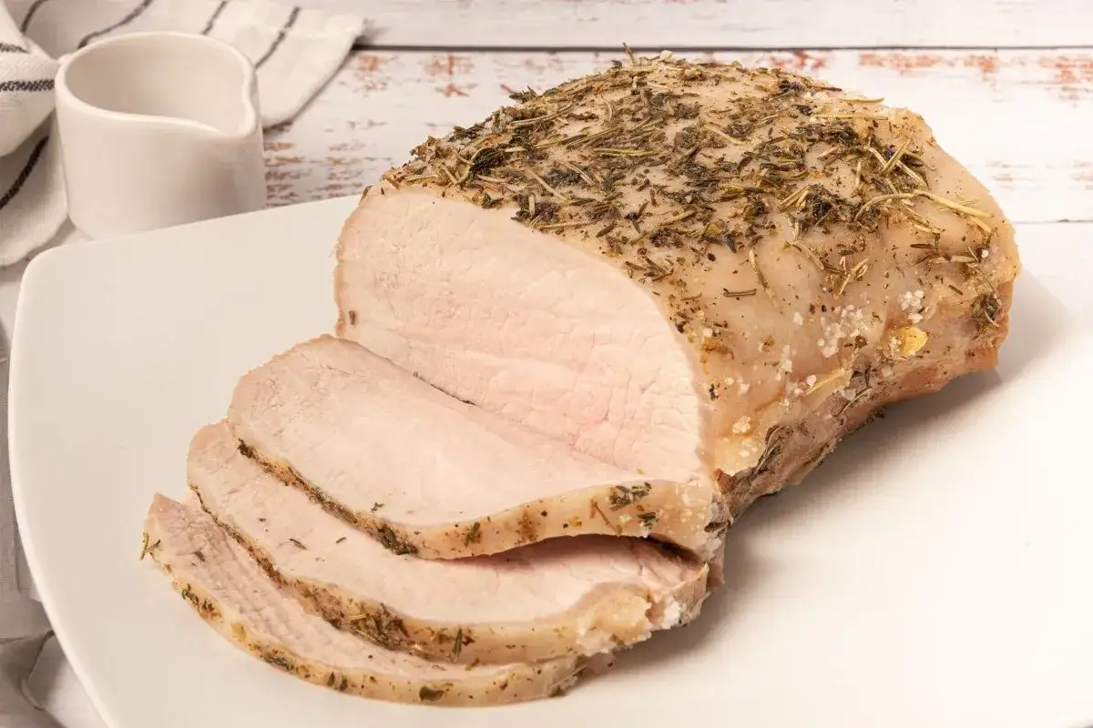 Lomo a la sal jugoso y tierno, cubierto de hierbas aromáticas, servido en una bandeja blanca con unas rodajas ya cortadas.
