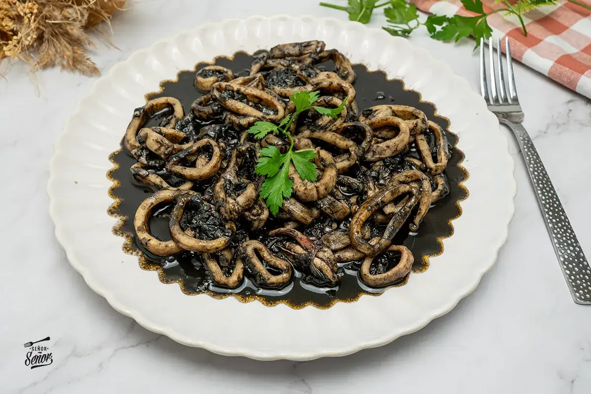 Calamares en su tinta, un plato tradicional español, servido en un plato blanco con un tenedor y perejil fresco.