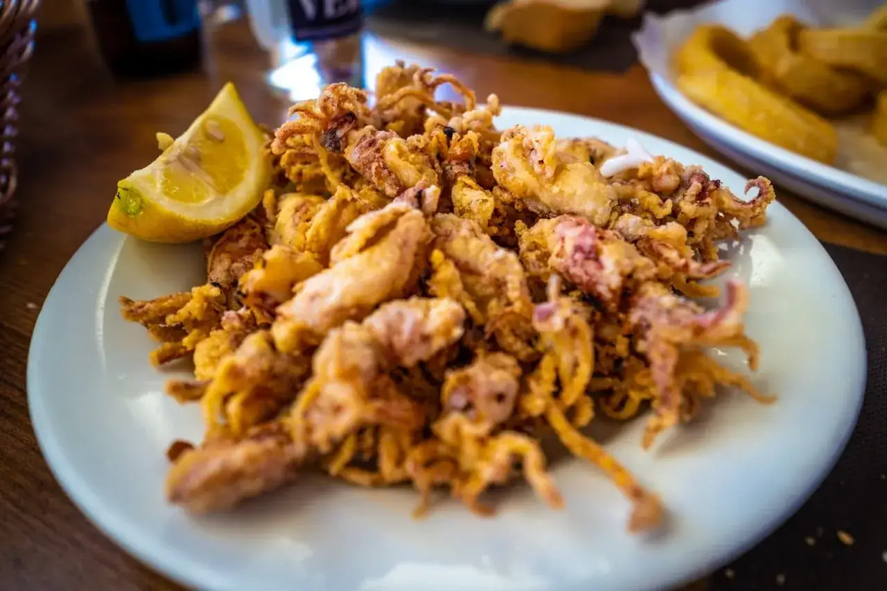 Un plato de puntillas de calamar crujientes y doradas, servido con una rodaja de limón fresco. ¡Un aperitivo perfecto!