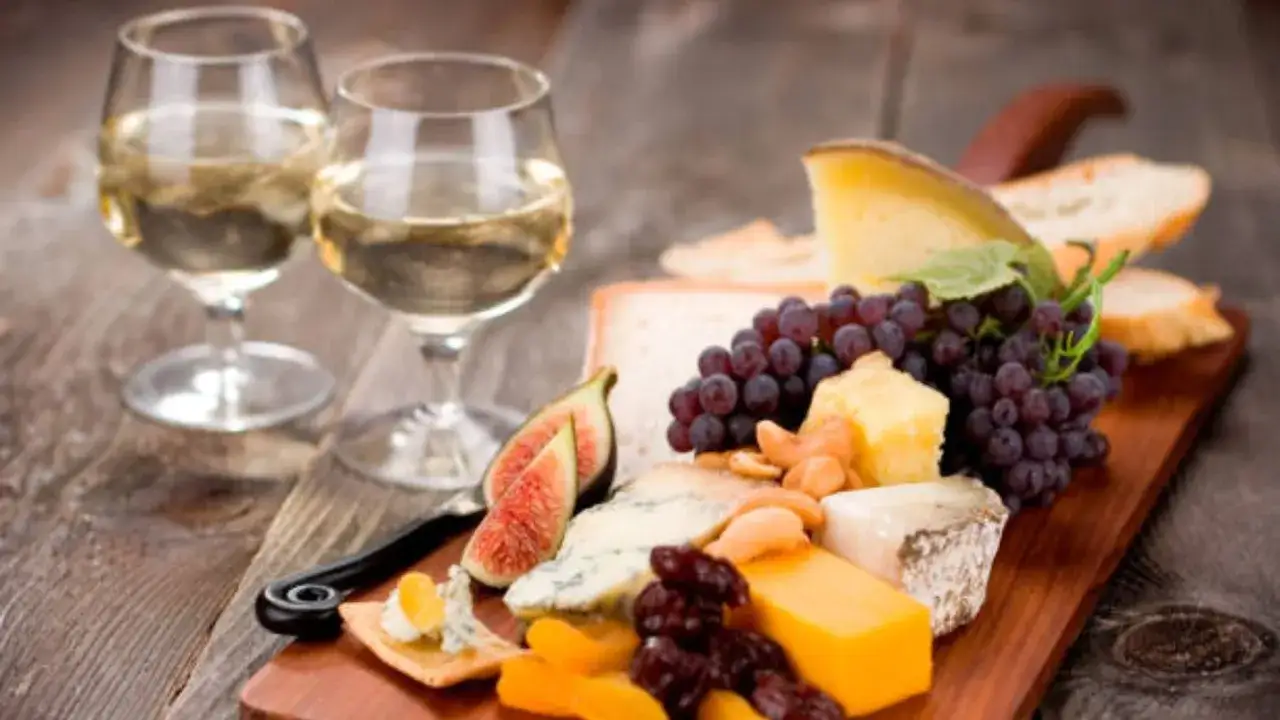 Tabla de quesos con uvas, higos y frutos secos, acompa&ntilde;ada de dos copas de vino blanco, ideal para maridar con un moscatel.
